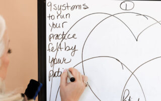 Coach Jennifer Pearce writing dental practice systems on a whiteboard during training session