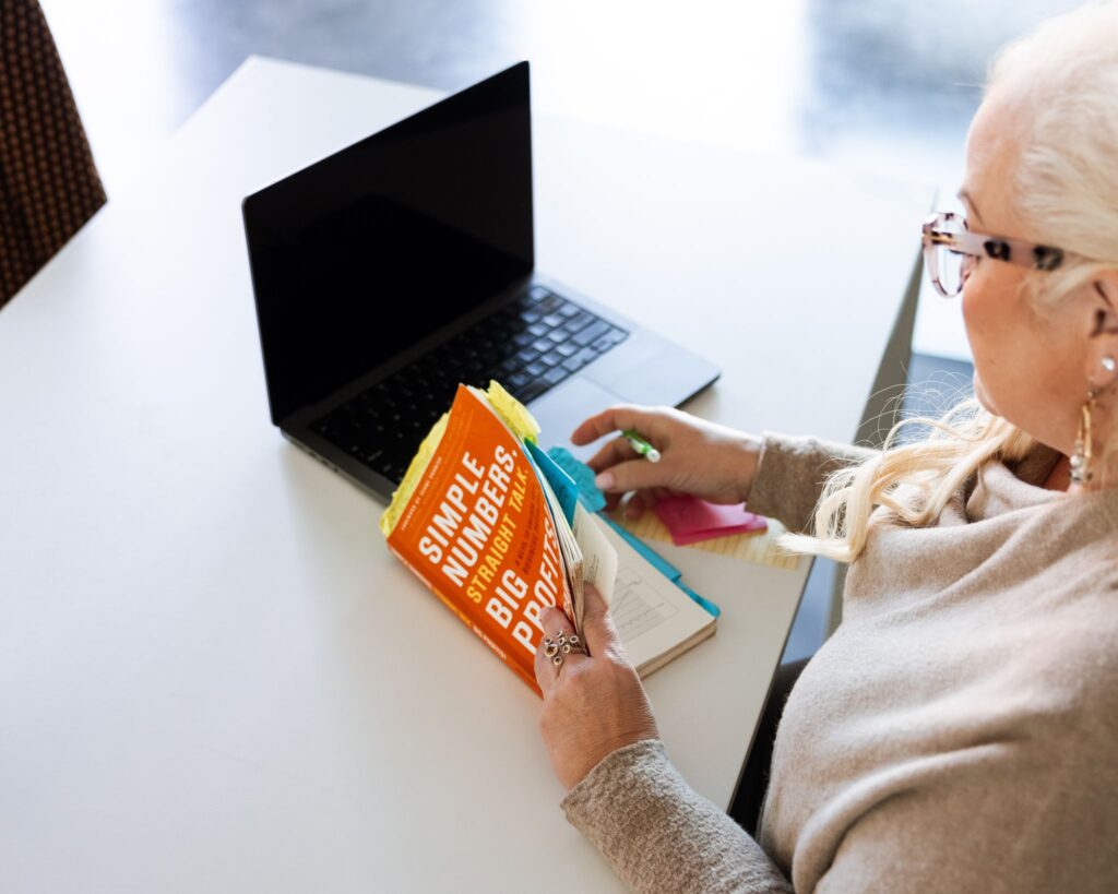 Dental practice owner reviewing business growth book while working on laptop